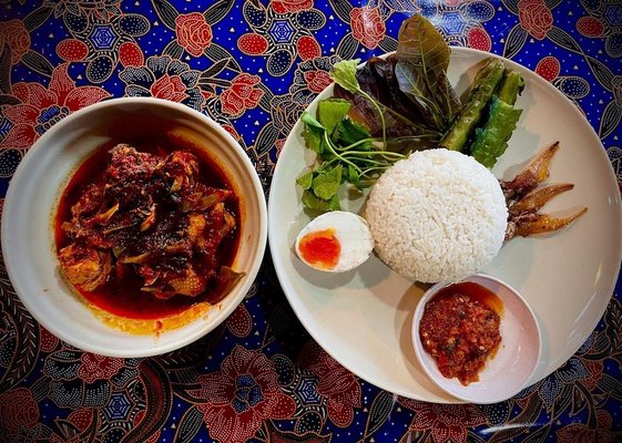 Asam pedas dengan nasi, ulam, telur dan sambal atas alas meja batik